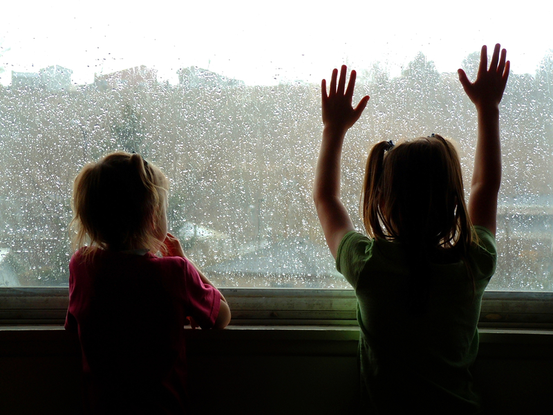Two kids looking out the window on a rainy day. 