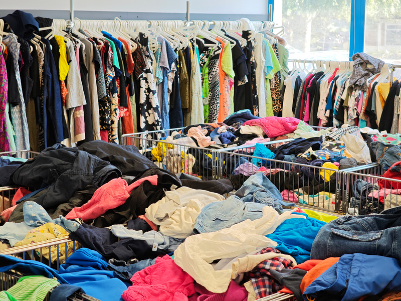 Second hand clothing store thrift shop interior with many heaps of used clothes in bins and colorful garments hanging on racks hangers, thrifting economy frugal fashion recycling shopping concept