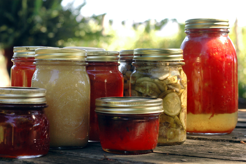 Homemade preserves sitting on a rustic table outside. Pickles, tomatoes, apple sauce, etc.