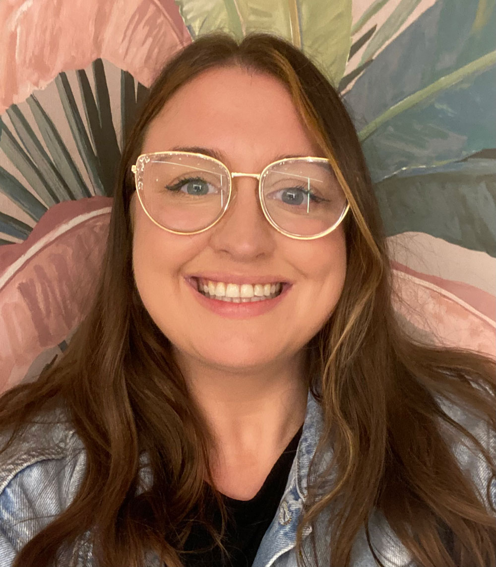Steph, founder of Bloom Play Studio, wearing clear-framed glasses and a denim jacket