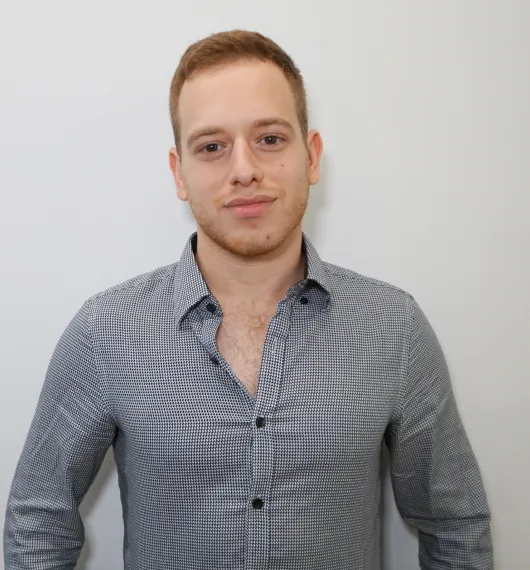 Young man with short light brown hair wearing a black and white checkered shirt against a plain white background.