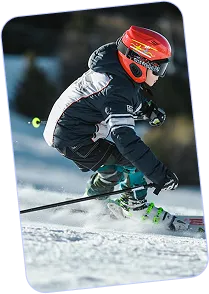 Child wearing red helmet and black ski outfit skiing downhill on snow.