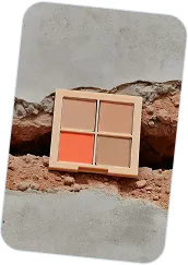Compact eyeshadow palette with four shades including beige, brown, and orange placed on a textured stone surface.
