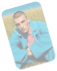 Blurred photo of a young man wearing a blue jacket sitting outdoors with greenery in the background.