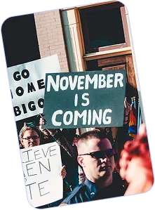 Protesters holding signs including one that reads 'NOVEMBER IS COMING' and others partially visible in a crowd.