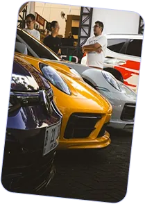 Front view of a row of luxury sports cars in black, yellow, and silver colors with three people standing and talking in the background.