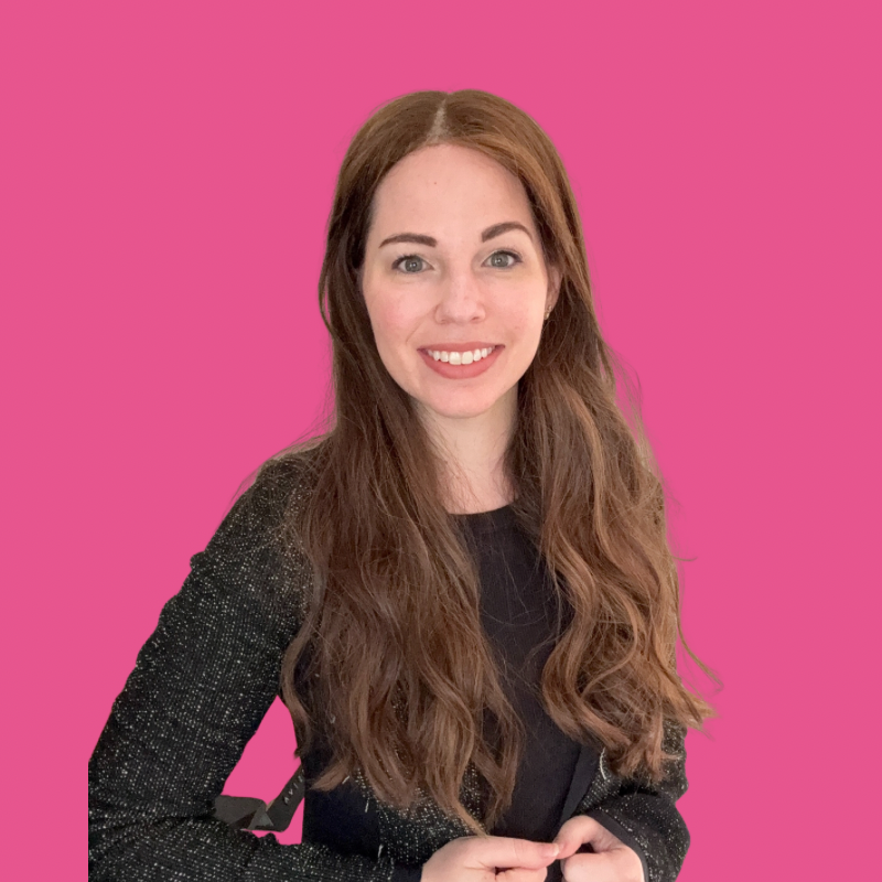 Smiling woman with long brown hair wearing a black top and sparkly black jacket against a solid pink background.