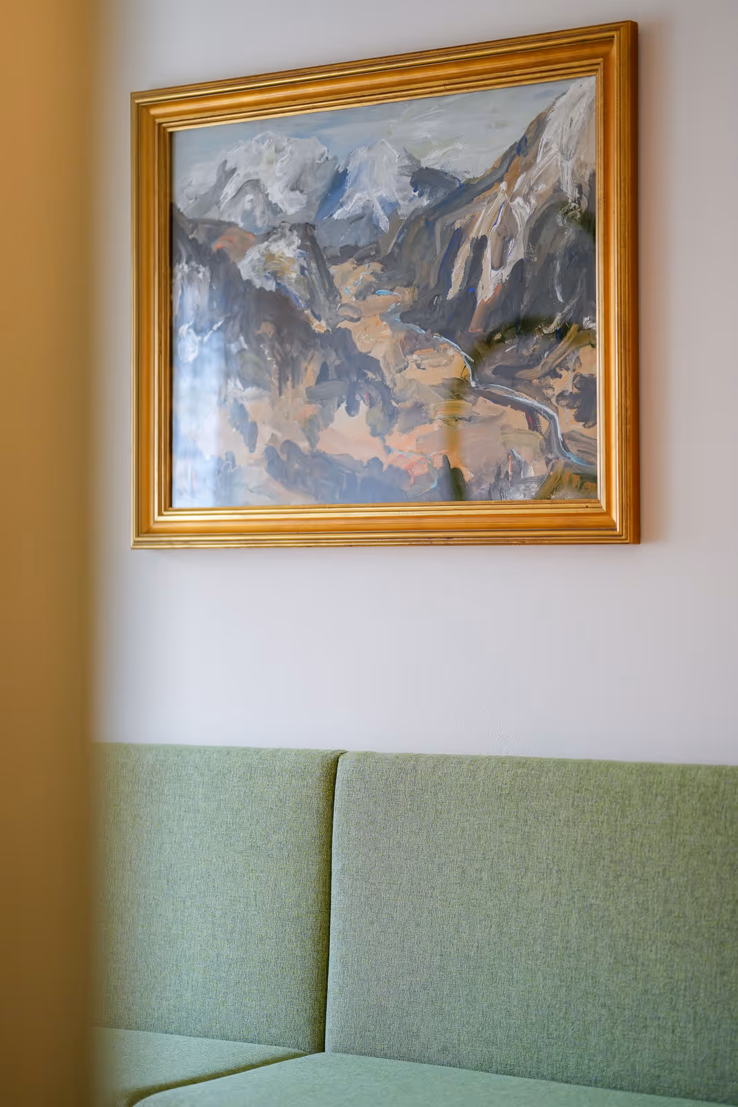 Gemälde eines Berglandschaftspanoramas mit Fluss, gerahmt in einem goldenen Rahmen, über einem grünen Sofa an einer weißen Wand.