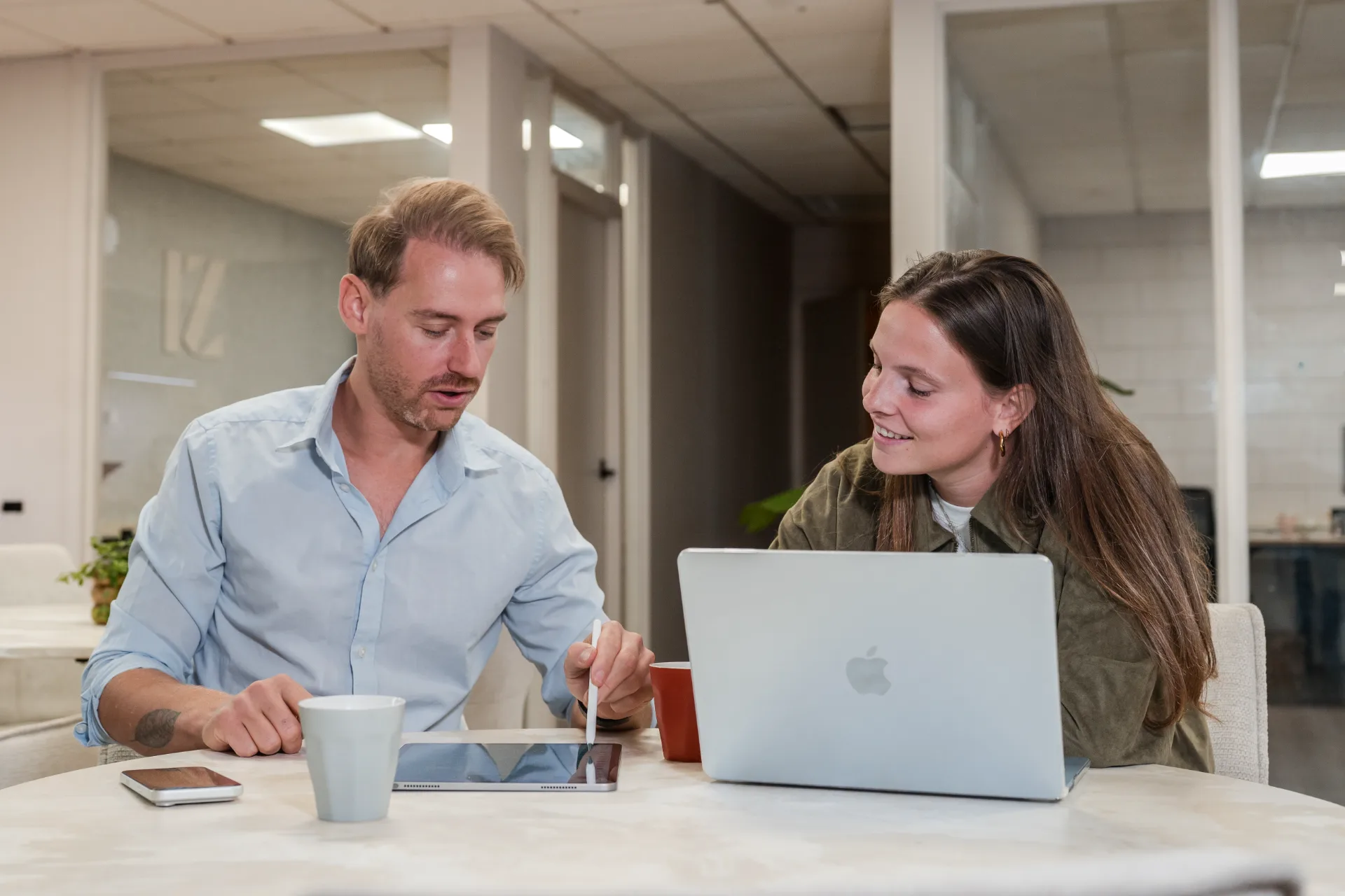 Twee collega's van De Zakerij overleggen aan tafel met tablet en laptop