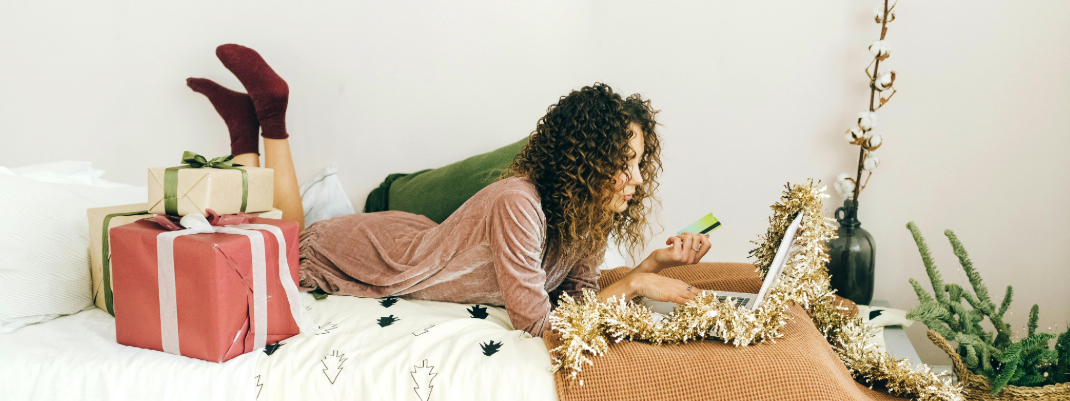 Nainen makaa sängyllä joulupakettien keskellä ja työskentelee kannettavalla tietokoneella