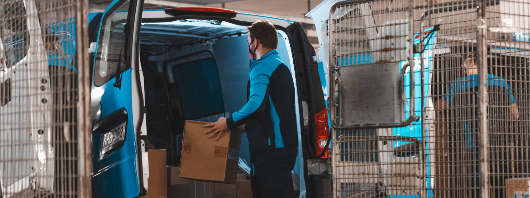 PostNordin kuljettaja kantaa pakettia pakettiautoon