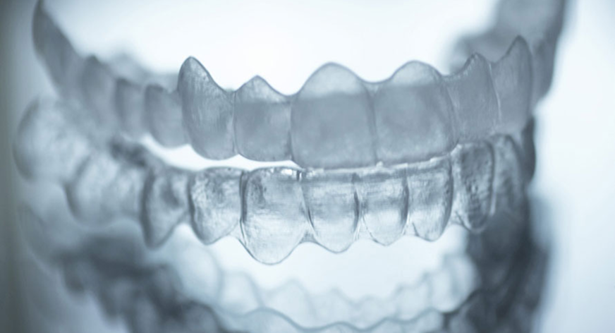 Nahaufnahme von transparenten Zahnschienen, die übereinander auf einer spiegelnden Oberfläche liegen.