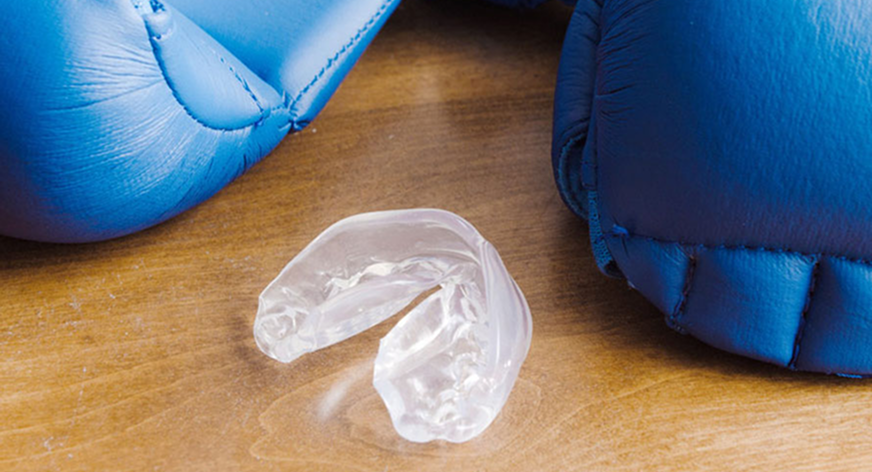 Transparenter Sportmundschutz auf einer Holzoberfläche zwischen zwei blauen Boxhandschuhen.