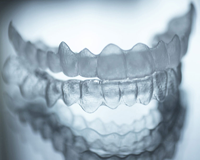 Nahaufnahme von transparenten Zahnschienen, die übereinander auf einer spiegelnden Oberfläche liegen.