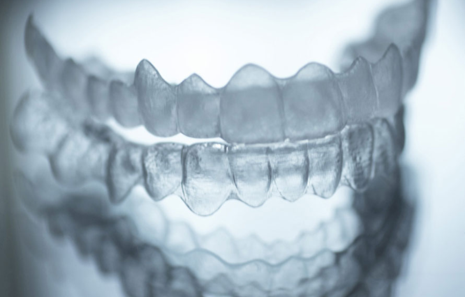 Nahaufnahme von transparenten Zahnschienen, die übereinander auf einer spiegelnden Oberfläche liegen.