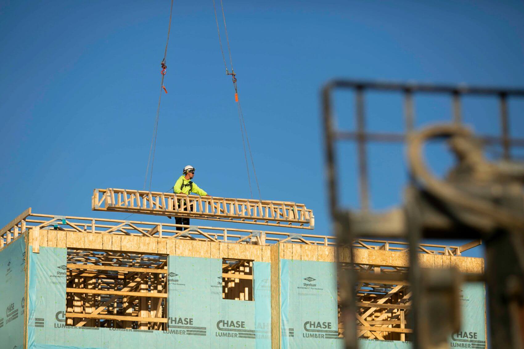 A commercial rough framing carpenter directs a boom while lowering a truss into place.