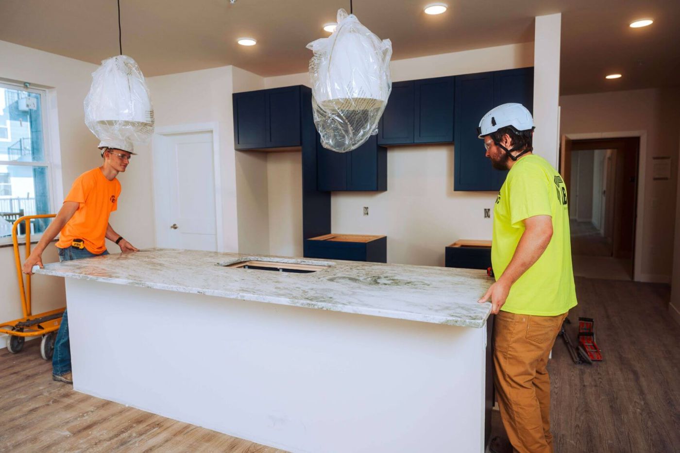 Two QBC installers setting a quartz island top in a multifamily kitchen