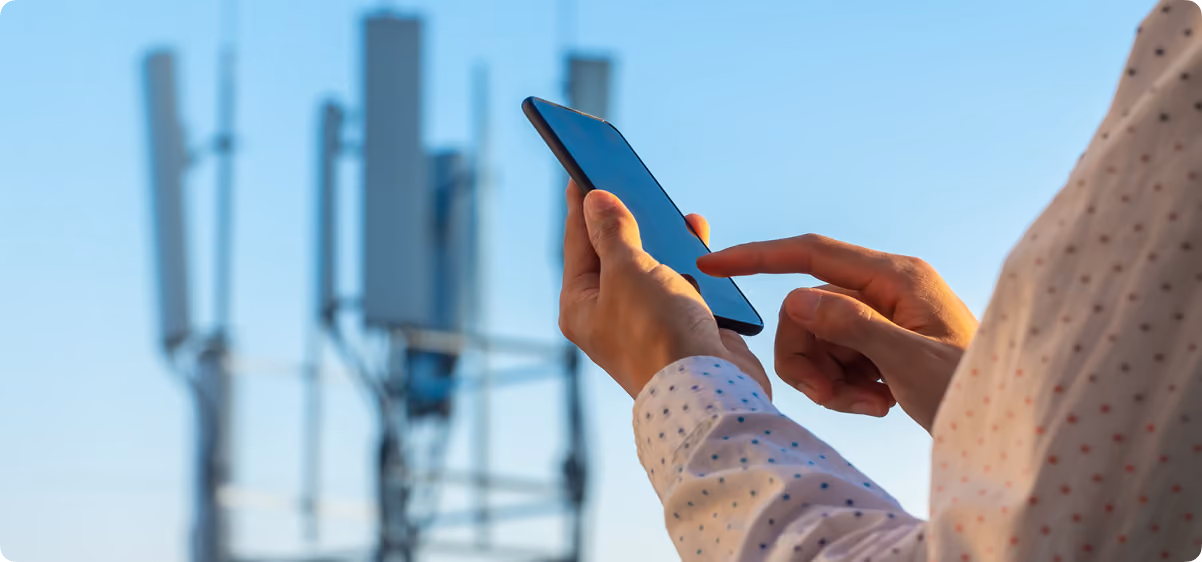 Person using a smartphone in front of cellular network towers