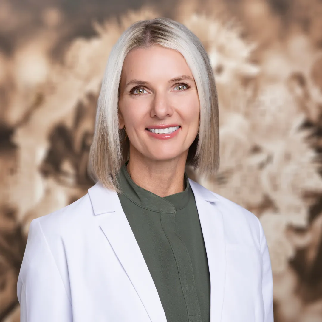 Dr Simpson - Dentist , Smiling woman with shoulder-length blonde hair wearing a white lab coat and green shirt.