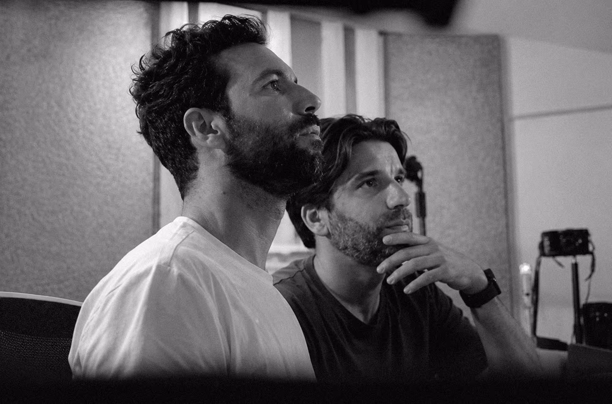 Two men with beards intently looking at something off-camera indoors.