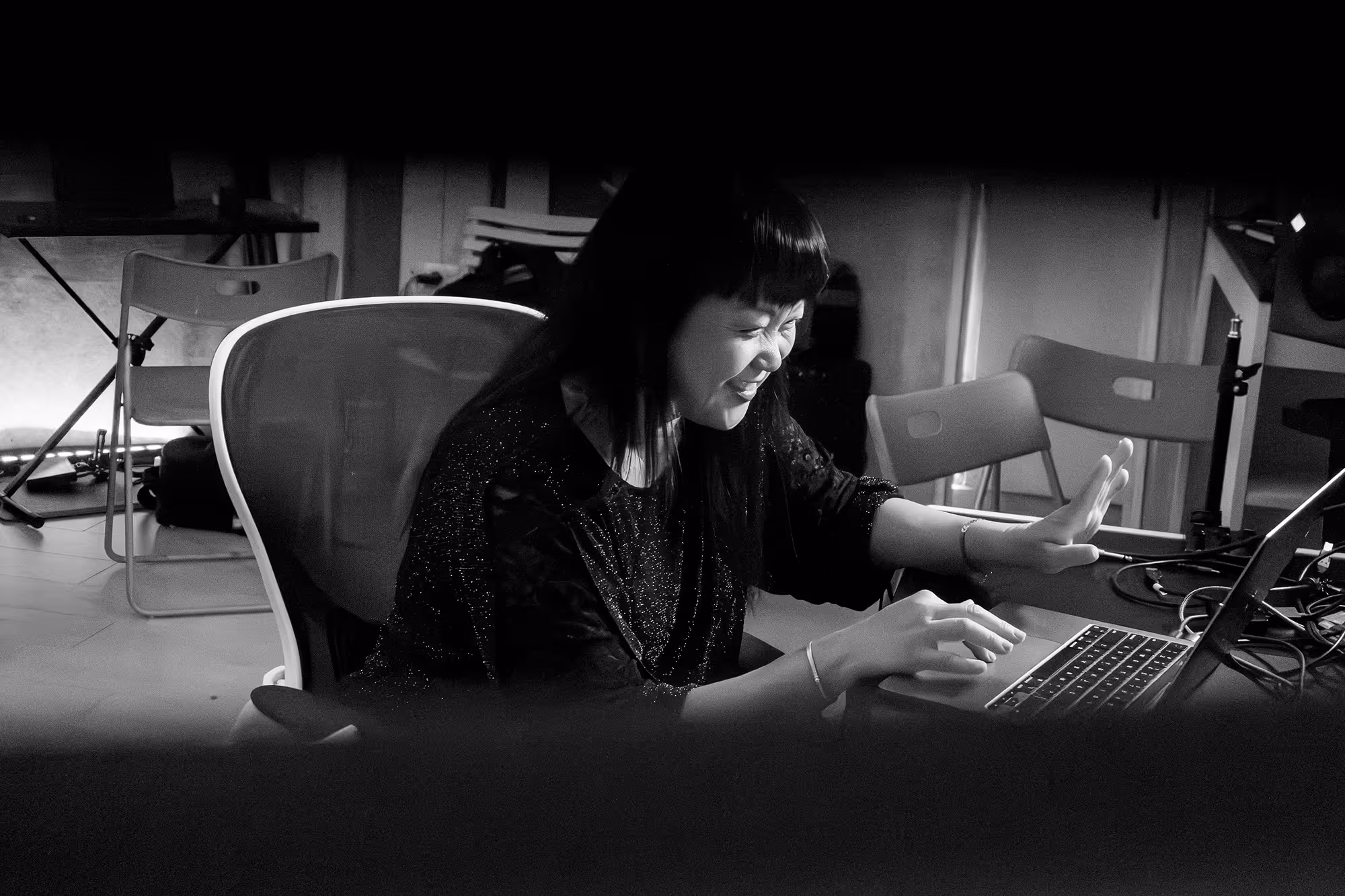 Woman smiling and interacting with a laptop in a room with chairs and equipment.