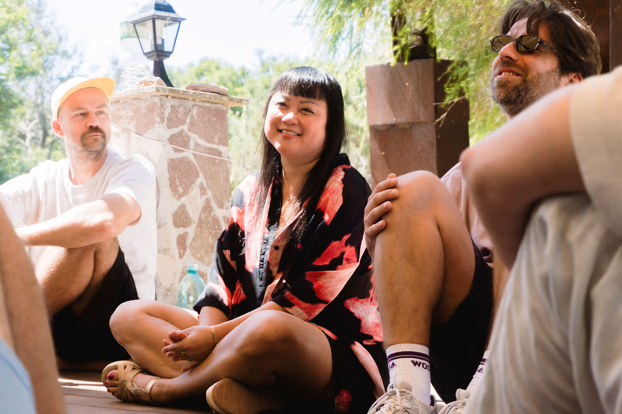 Three people sitting outdoors on a porch, one woman smiling at the camera.