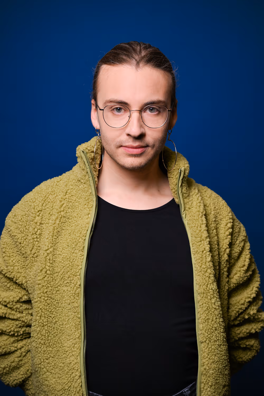 Close-up of a person with curly hair and neutral expression against dark background.