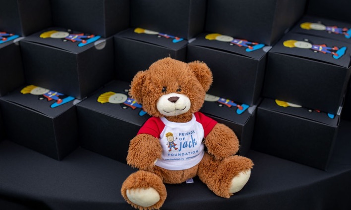 A Friends of Jack Foundation teddy bear sitting among rows of event gift boxes