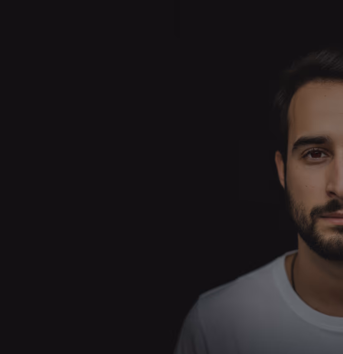 Close-up of the right side of a young man's face with a beard against a black background.