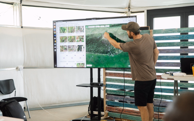 A man pointing with left hand to the digital screen where a platform shows photo evidence submitted by planters in Kenya
