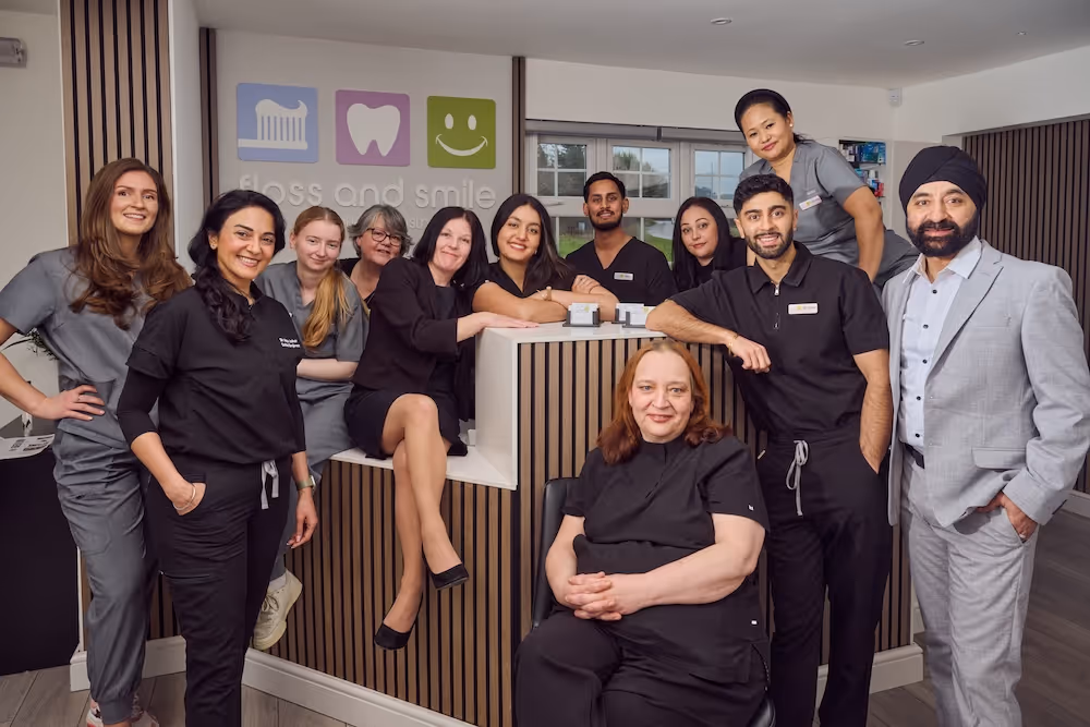 A diverse group of twelve dental clinic staff posing together inside a modern reception area with a 'floss and smile' sign on the wall.