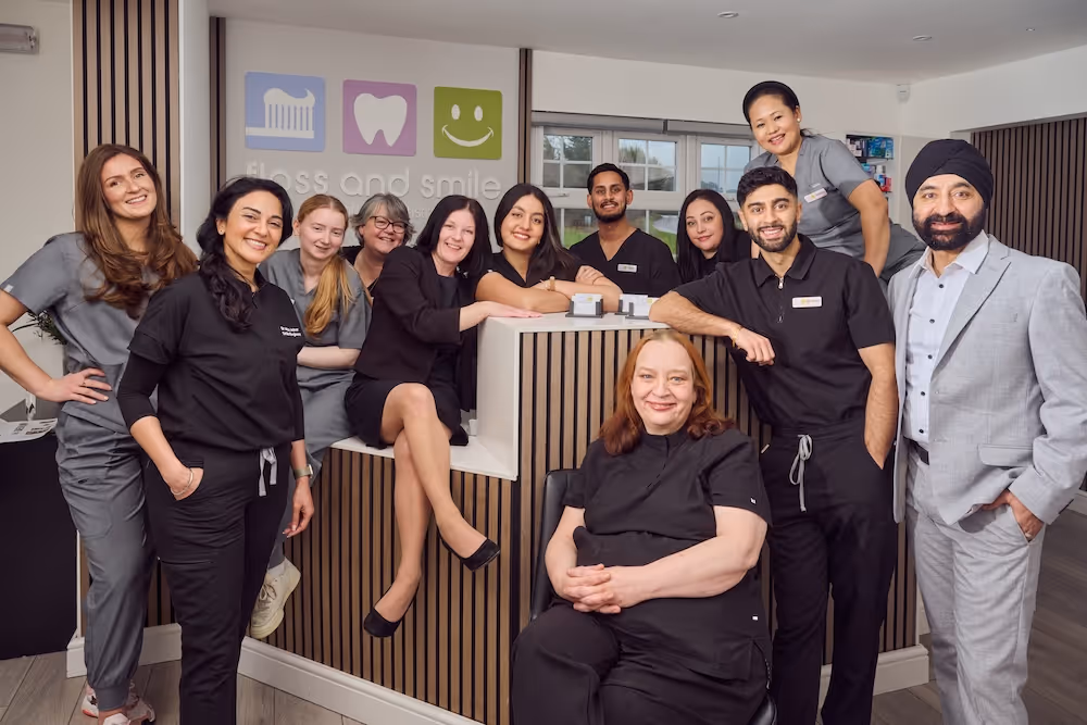 Group of dental clinic staff posing inside the clinic with a sign showing a toothbrush, tooth, and smiling face icons on the wall.