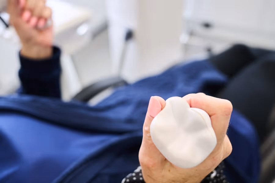 Close-up of a person squeezing a white, tooth-shaped stress ball while sitting down.