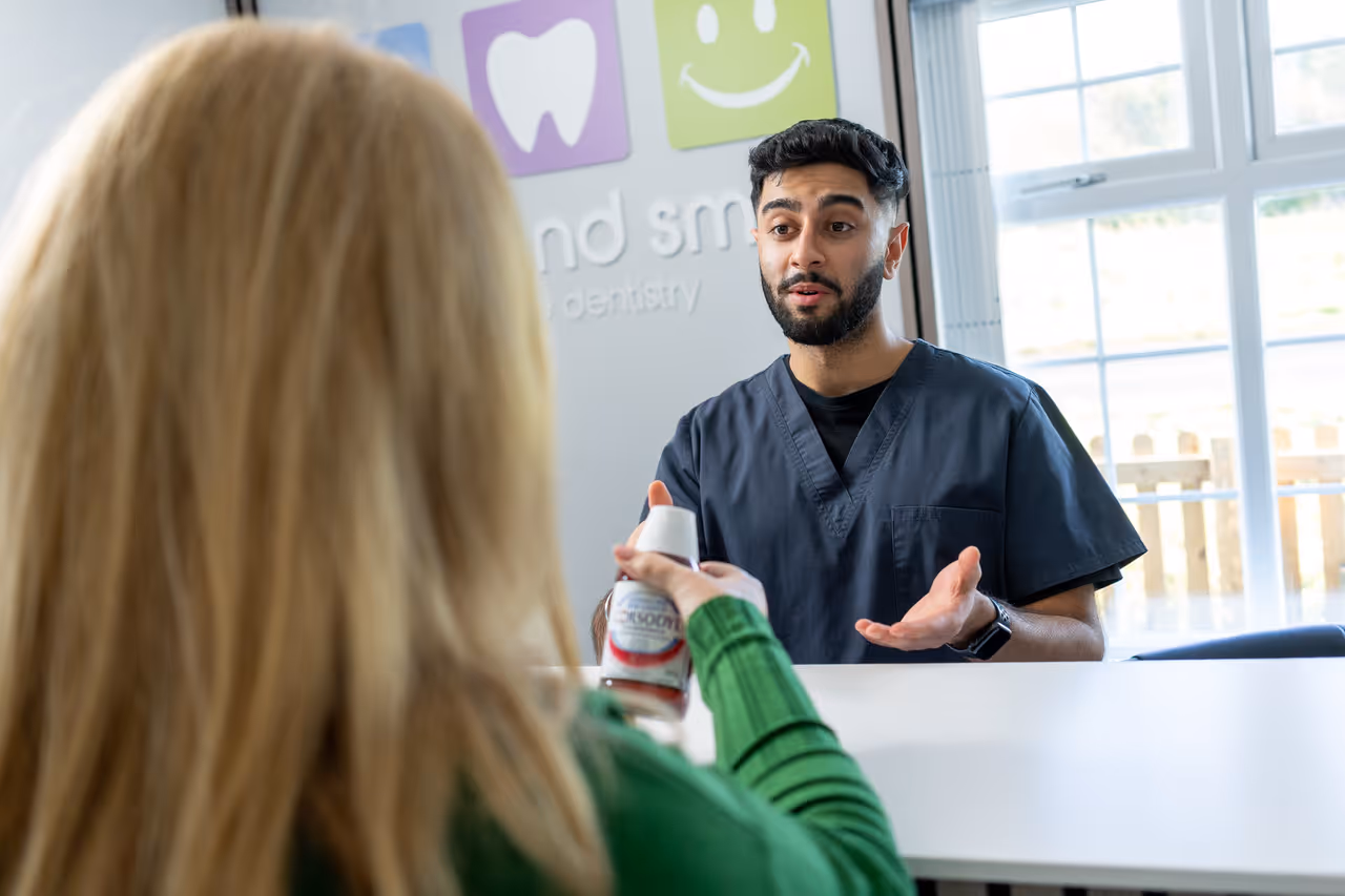 Dentist explaining a dental product to a woman holding a bottle in a dental clinic reception area.