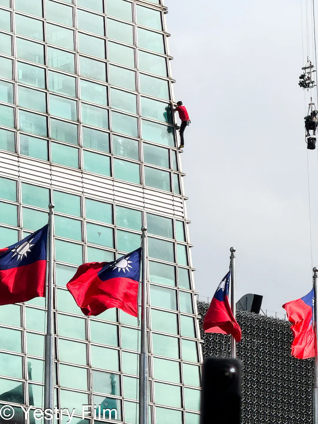 2026年 Alex Honnold 徒手攀登台北 101 大樓側影紀錄，畫面包含台北 101 玻璃帷幕、中華民國國旗與攀登者。