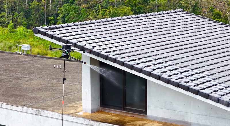 專業無人機進行高空建築玻璃帷幕清洗作業，以高壓噴灑技術取代傳統人力，提升作業安全性與效率。