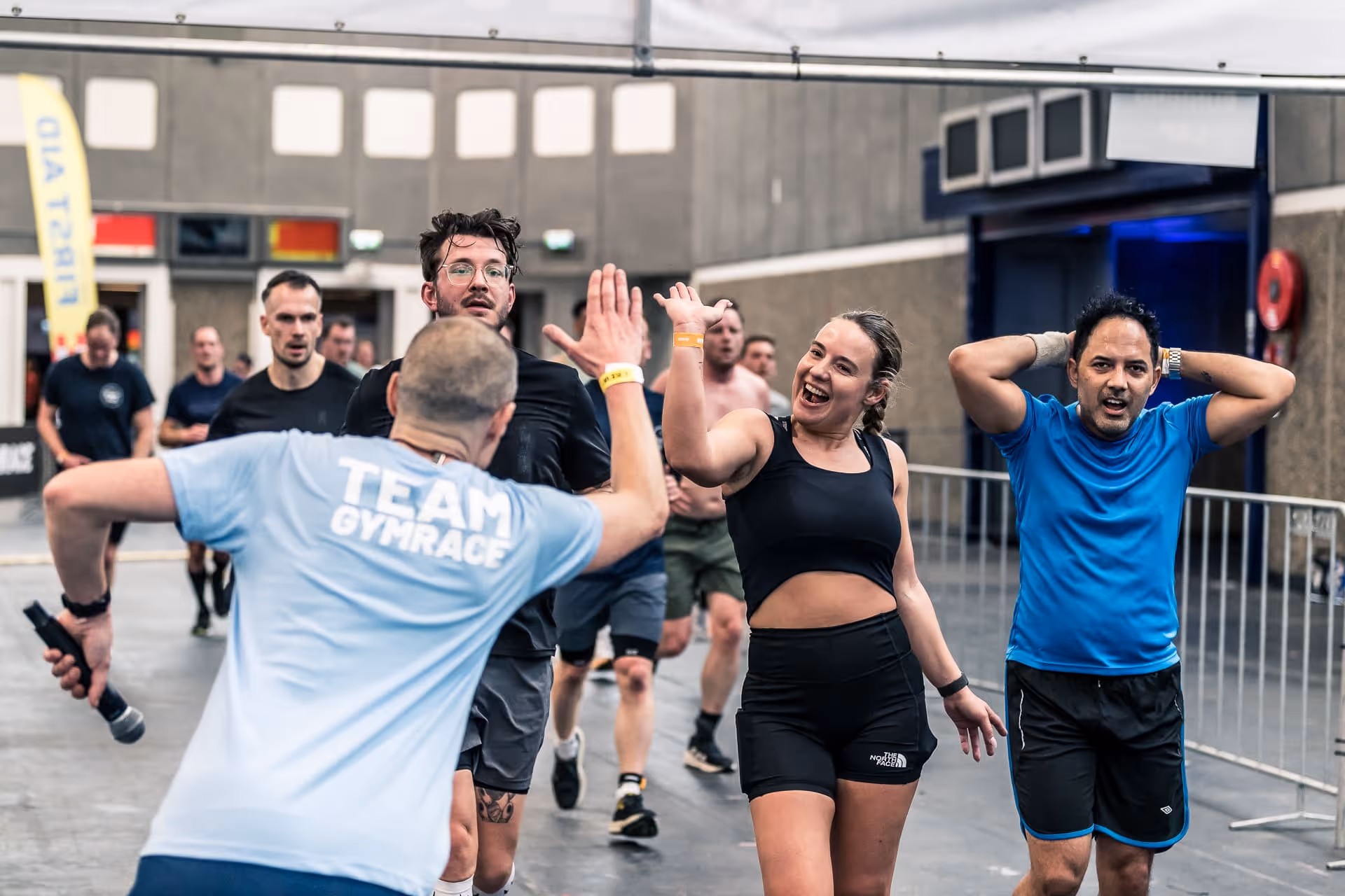 Runners giving high fives and stretching indoors during a race event with cheering participants behind.