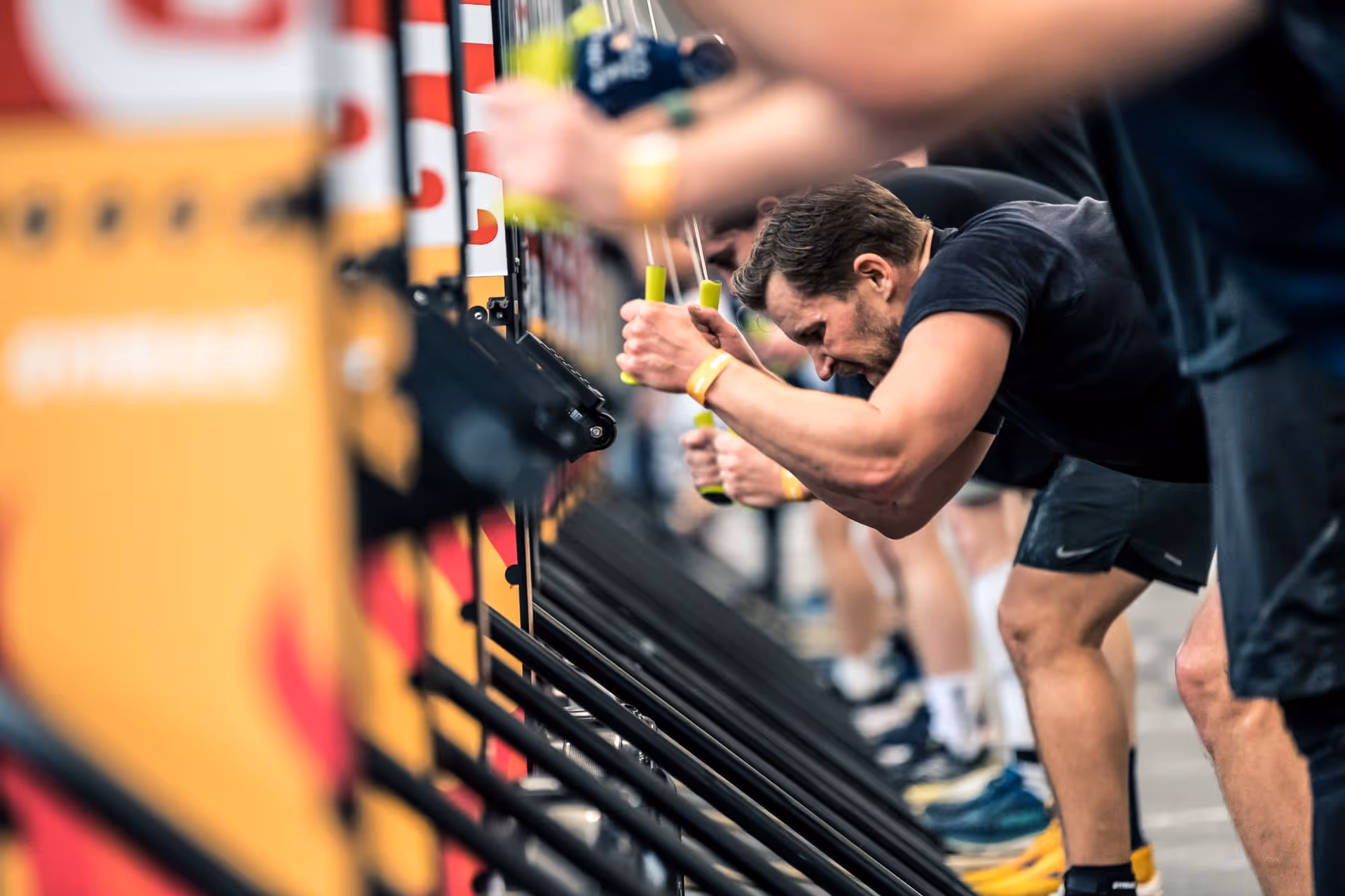 Men intensely rowing on indoor rowing machines lined up in a gym or fitness event.