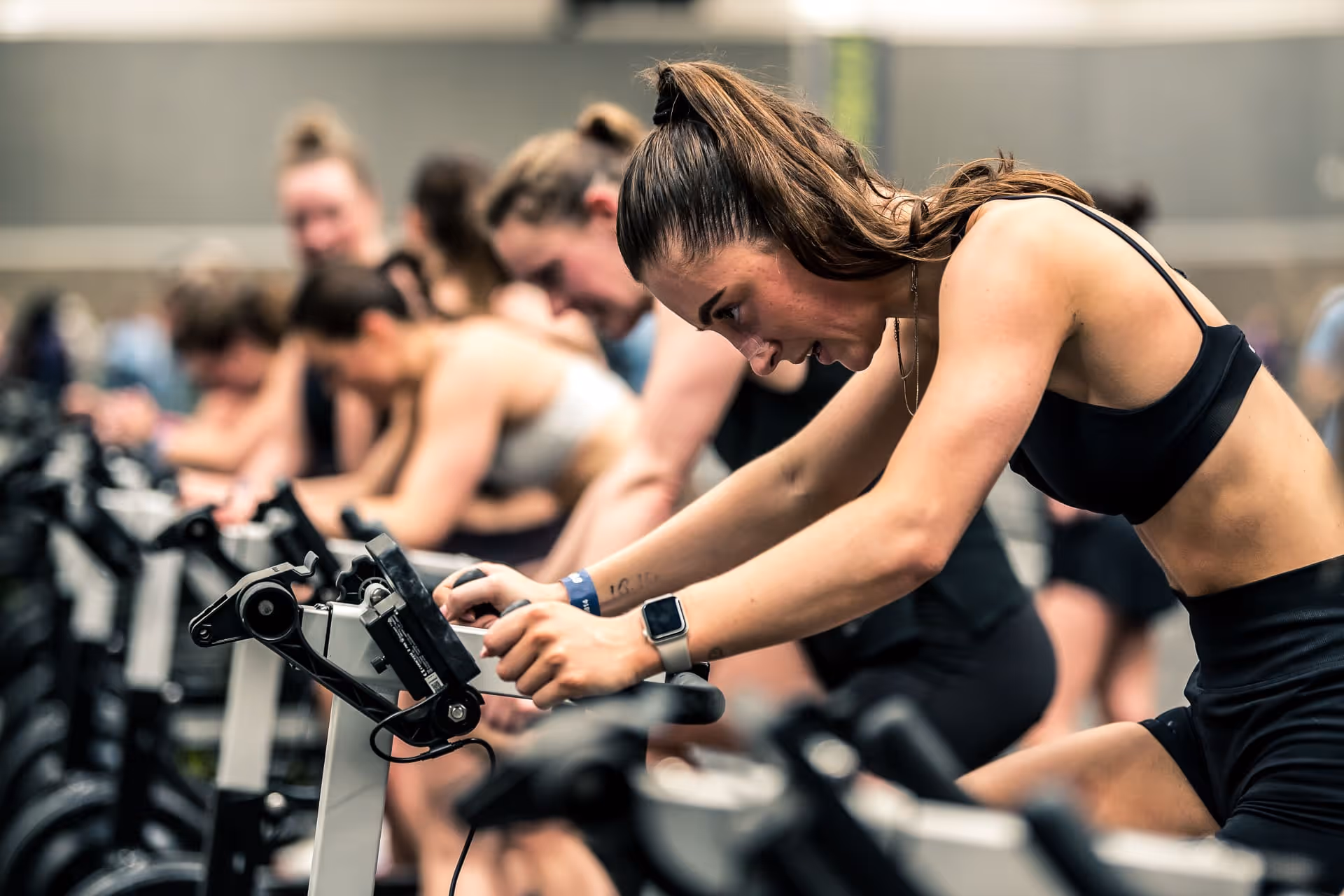 Woman in black sportswear intensely exercising on a stationary bike in a spin class.