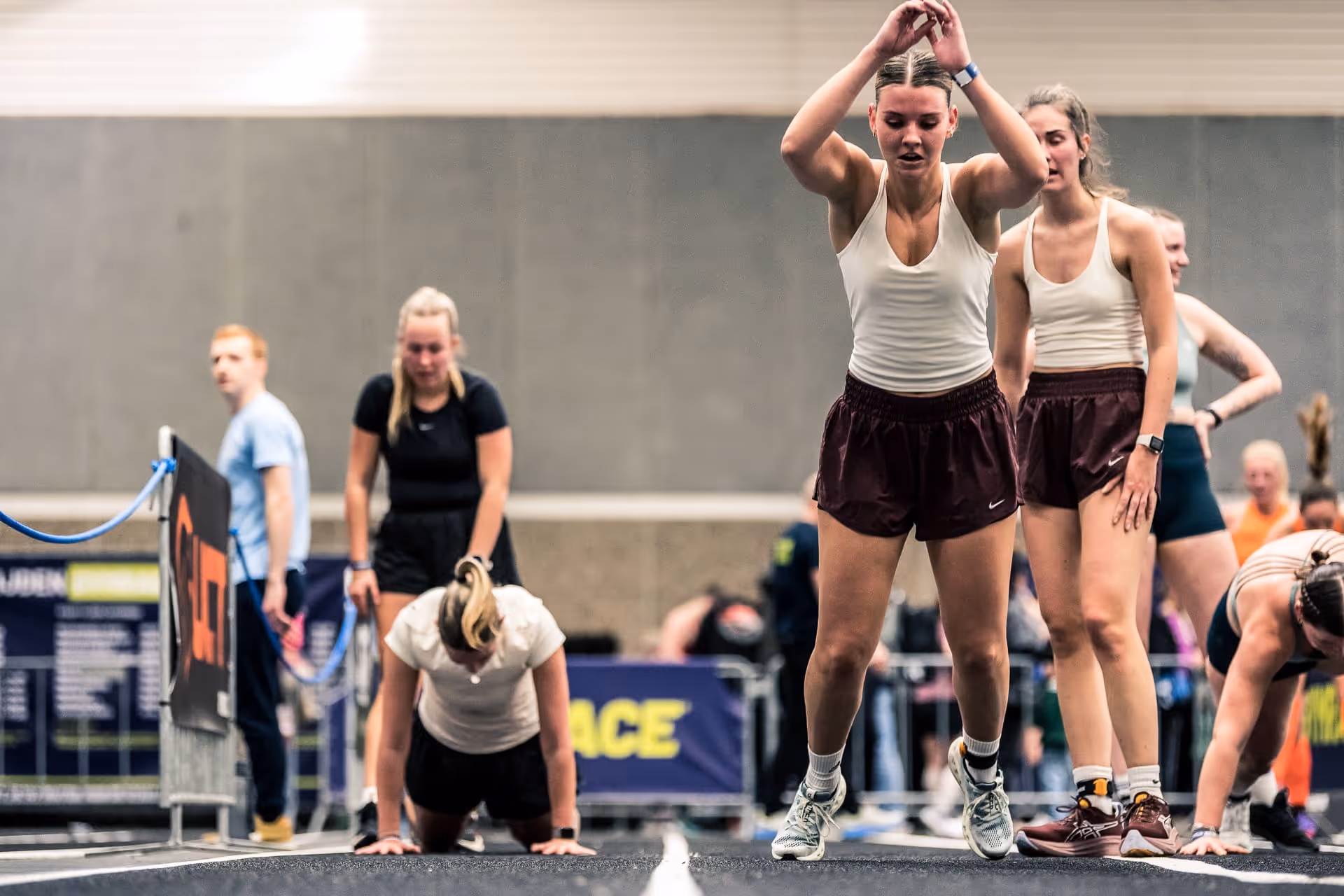 Group of young women in athletic wear performing burpees indoors during a fitness event.