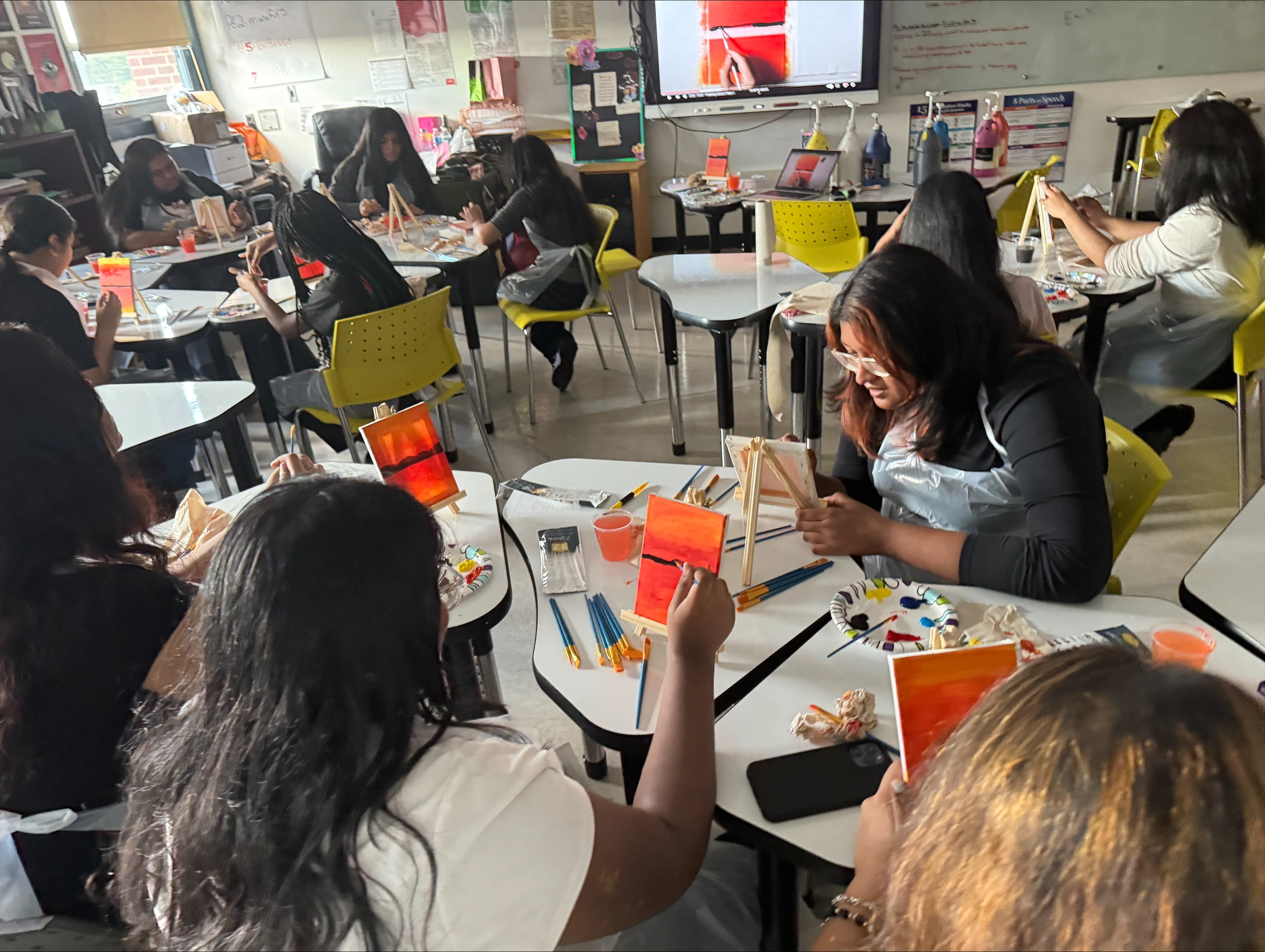 Students painting orange canvases on easels during art class
