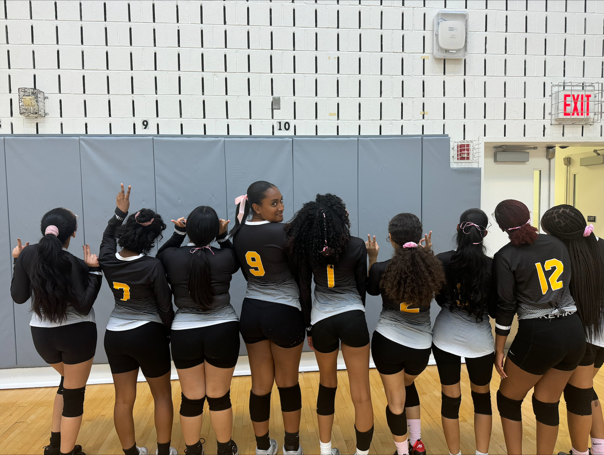 Girls volleyball team posing together in gym wearing black uniforms