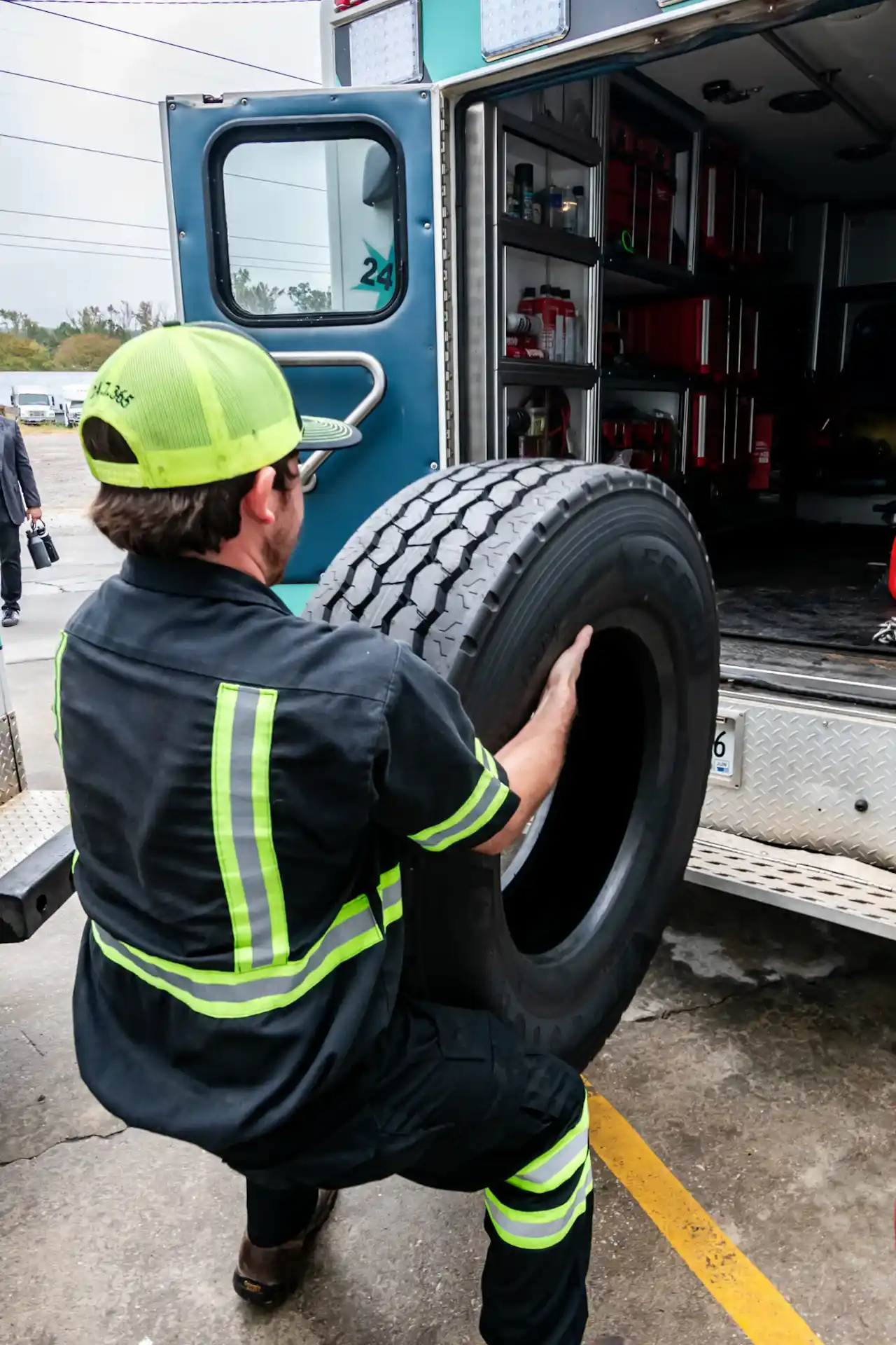 Tire service technician loading a commercial truck tire into a fully stocked roadside service truck for heavy-duty repairs.