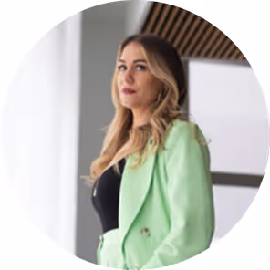 Portrait of a woman with long blonde hair wearing a light green blazer, looking confidently to the side indoors.