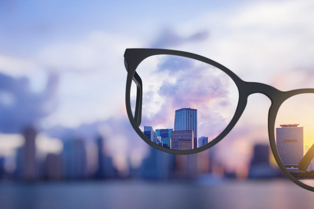 City skyline in clear focus seen through the lens of black-rimmed eyeglasses with a blurred cityscape background.