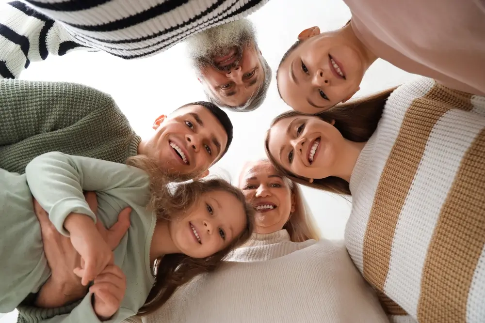 Smiling multigenerational family of six, including a young girl, looking down at the camera in a close circle.