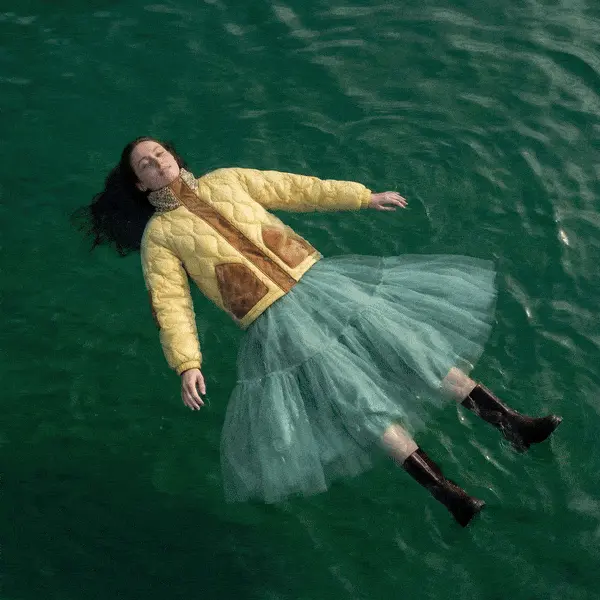 Woman wearing a yellow jacket and green skirt floating relaxed on calm water with eyes closed. Made with The Fabricant Image-To-Video tool