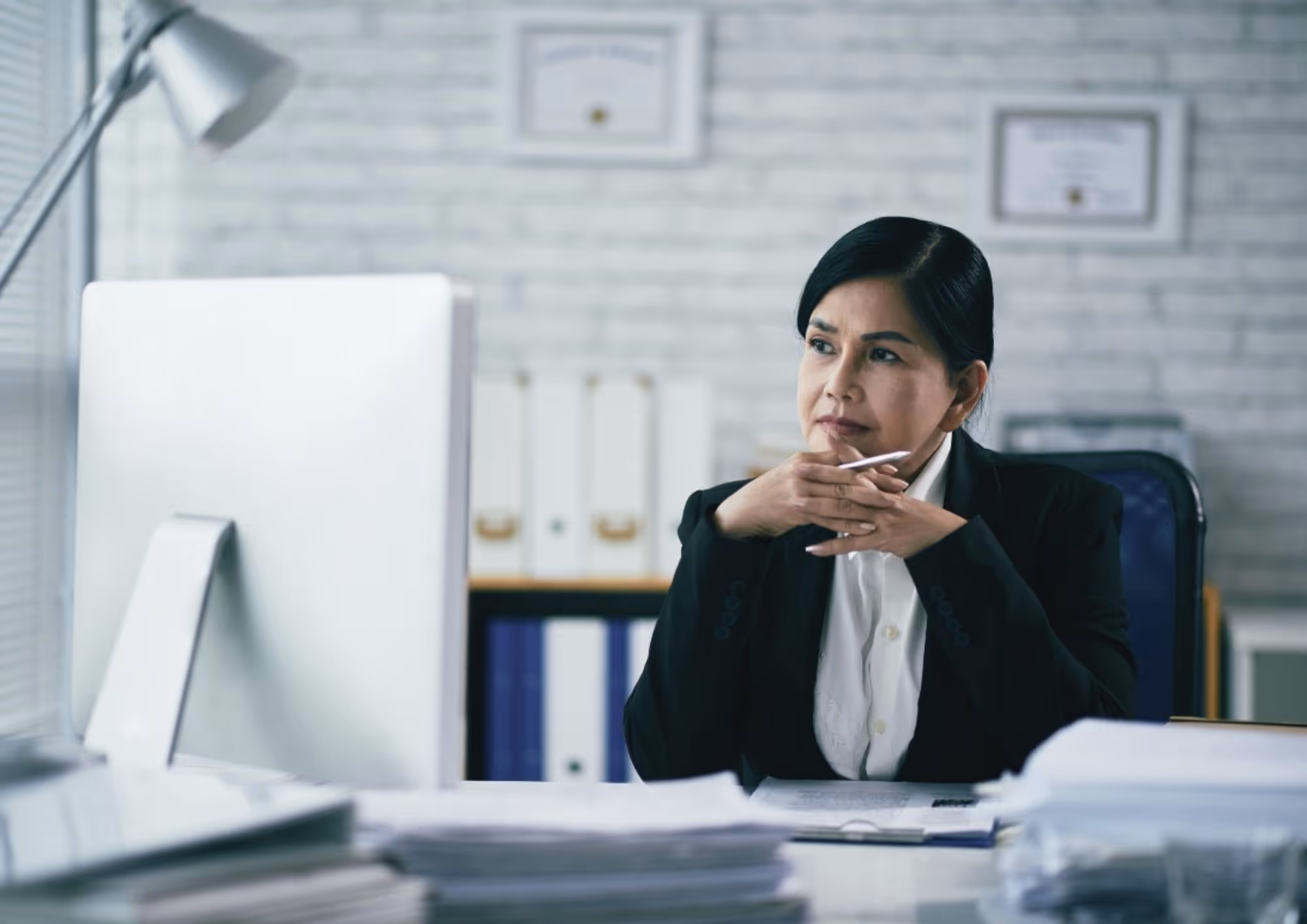 A lawyer with her hair pulled back sits in a clean, minimal white office, and hesitates in front of her computer screen while writing a blog post.