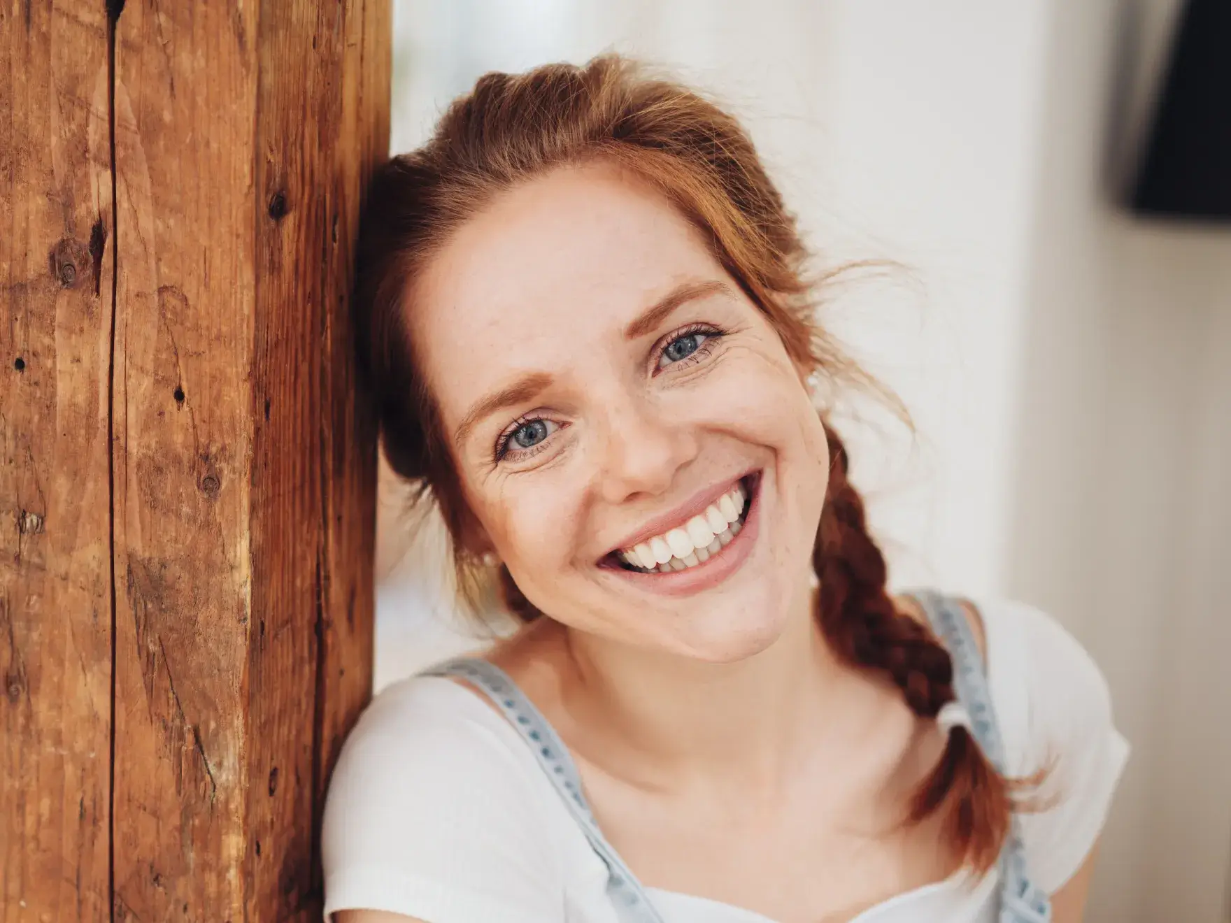 A smiling woman leaning against a wooden wall.