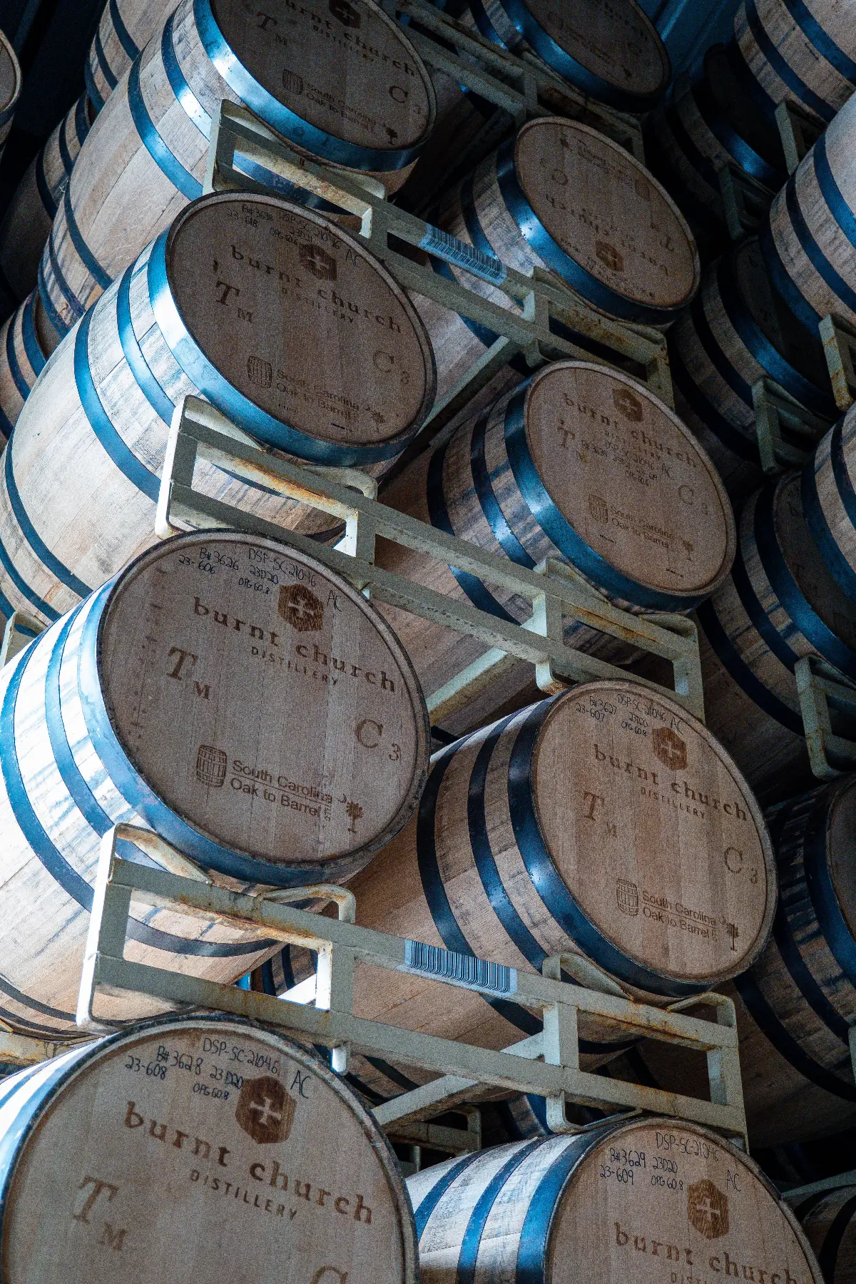 Stacked wooden barrels labeled 'burnt church distillery' with metal hoops inside a storage rack.